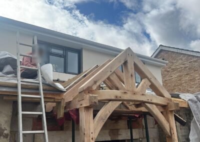 Green oak-frame porch trusses being installed on an extension